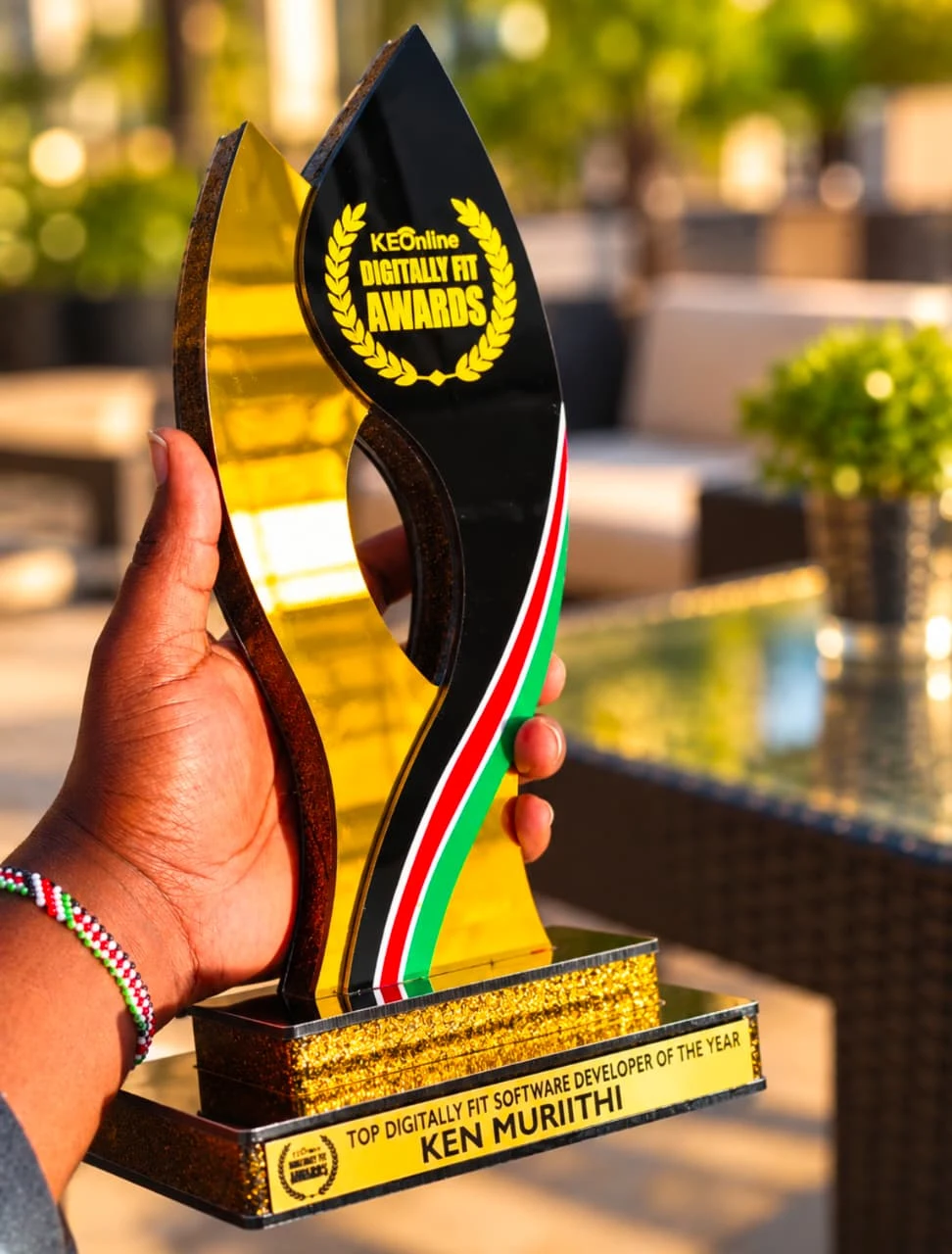 A hand holding Ken Murithi’s Top Digitally Fit Software Developer of the Year trophy, with Kenyan flag colours along its edge